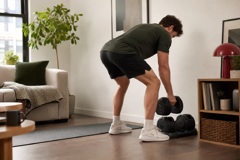 An adult using dumbbells in a bright, compact training space