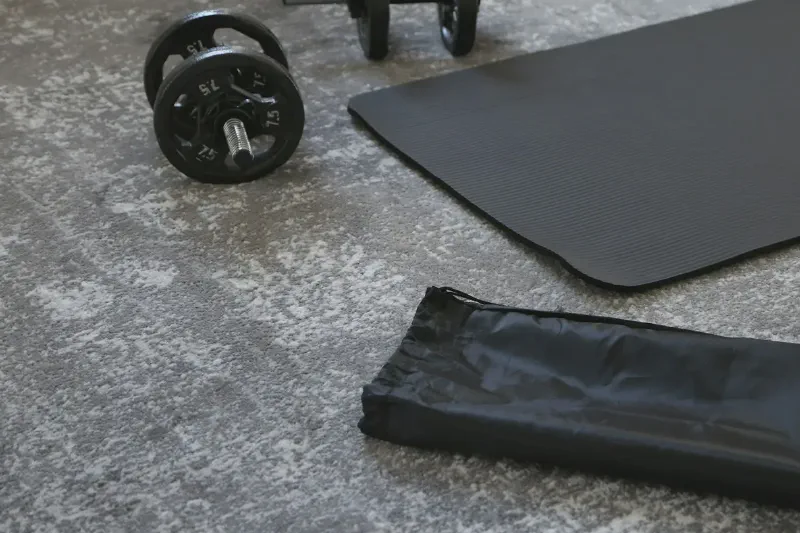 A compact home strength-training setup with dumbbells stored neatly beside an exercise mat in a small apartment