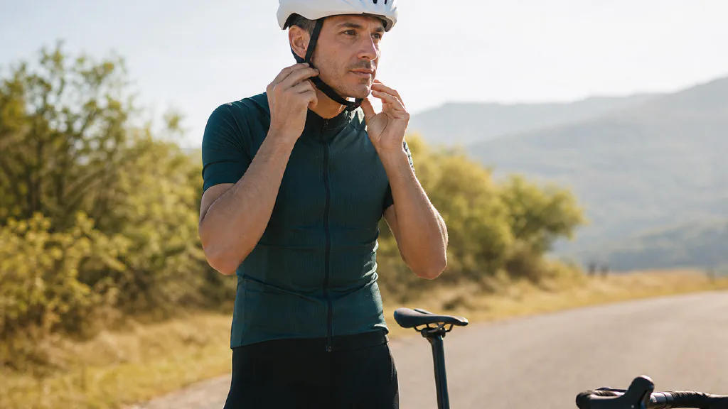 A recreational road cyclist adjusting the chin straps of an unbranded helmet